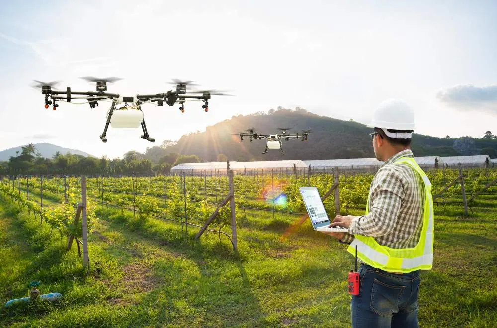 Χειριστής με tablet δίπλα σε αμπέλι, ενώ drones πετούν πάνω από τις σειρές